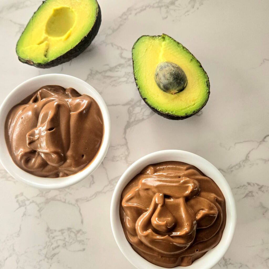 Chocolate Avocado Pudding (Keto Friendly) Chocolate avocado pudding in small white bowls on a marble surface.