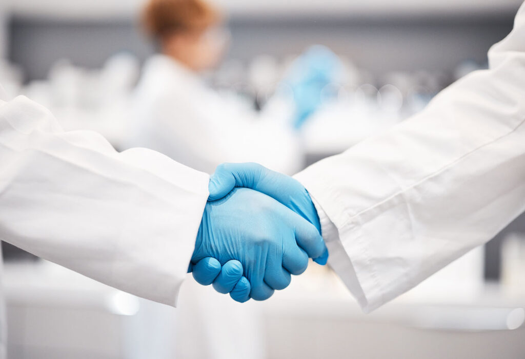 two people in lab coats shaking hands